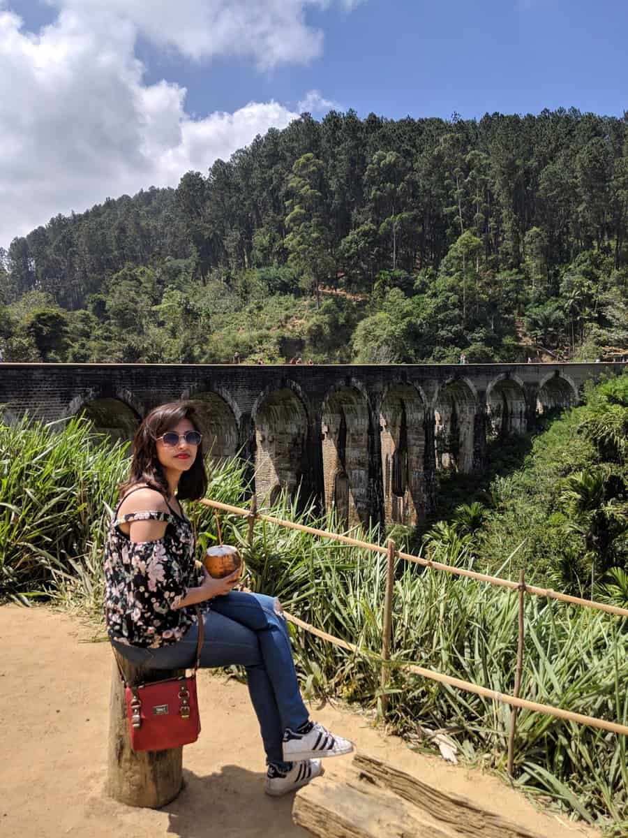 Girl having coconut with nine arches bridge in the background - things to do in ella sri lanka