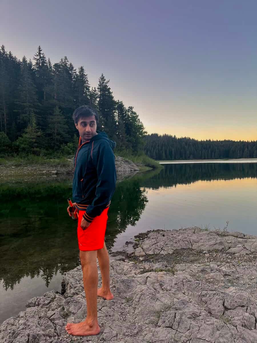A man stands at the edge of Black Lake in Durmitor National Park, looking back over his shoulder as the warm colours of sunset reflect across the calm water. The peaceful mountain setting captures the quiet atmosphere that makes Black Lake (Lake Jzero) one of the park's most memorable places to visit.