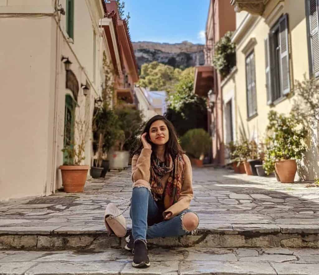 A woman sits on stone steps in Athens, surrounded by historic architecture and the city's timeless streetscape. The relaxed scene captures a quiet moment while exploring one of Greece's most iconic destinations.