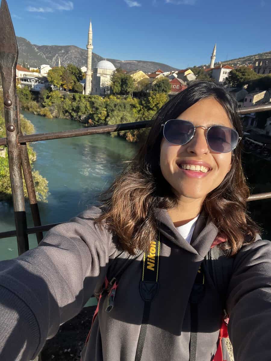 A selfie of a traveler standing on the historic Stari Most bridge in Mostar, Bosnia and Herzegovina. The stone arch bridge and the turquoise Neretva River create a scenic backdrop that highlights one of the city's most recognizable landmarks.
