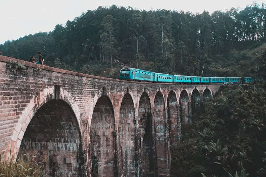 A blue train traverses the iconic Nine Arch Bridge in Ella, surrounded by lush Sri Lankan forests.