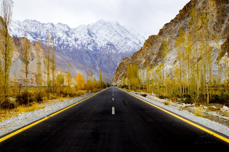 things to do in Hunza Valley is drive on a road surrounded by autumn trees and snow-covered mountains