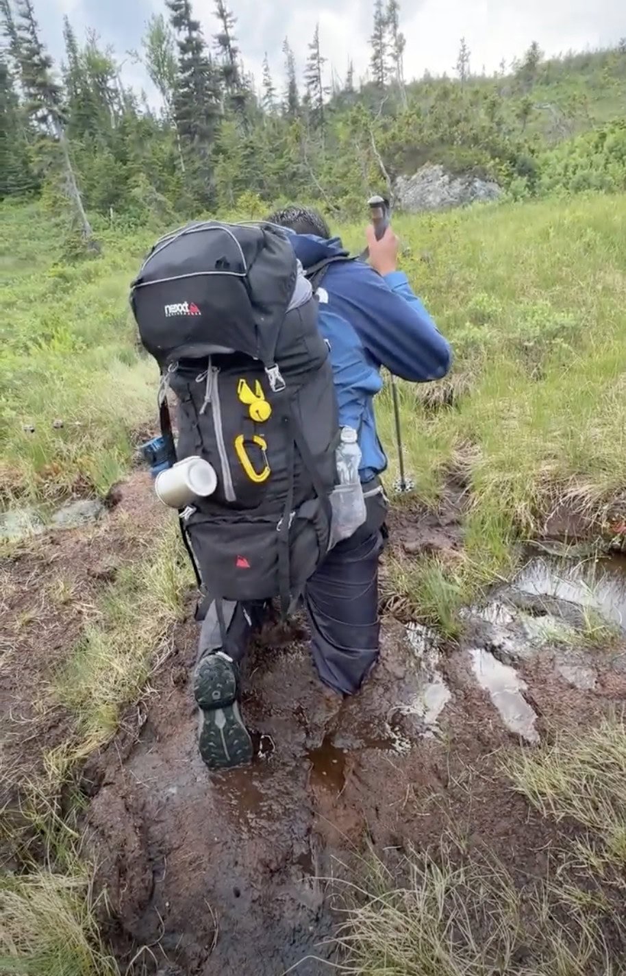 A man thigh deep in mud, his back is towards the frame emphasizing the muddy conditions of the long range traverse trail.