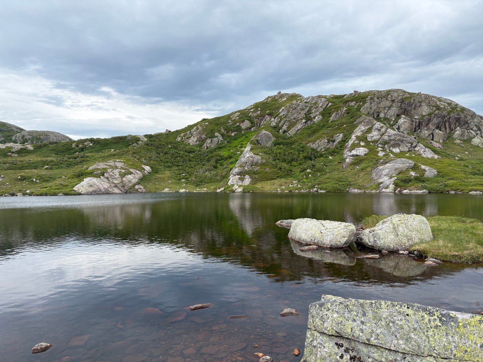 One of the many expansive lakes along the Long Range Traverse, surrounded by low vegetation and distant ridgelines under a cloudy sky.