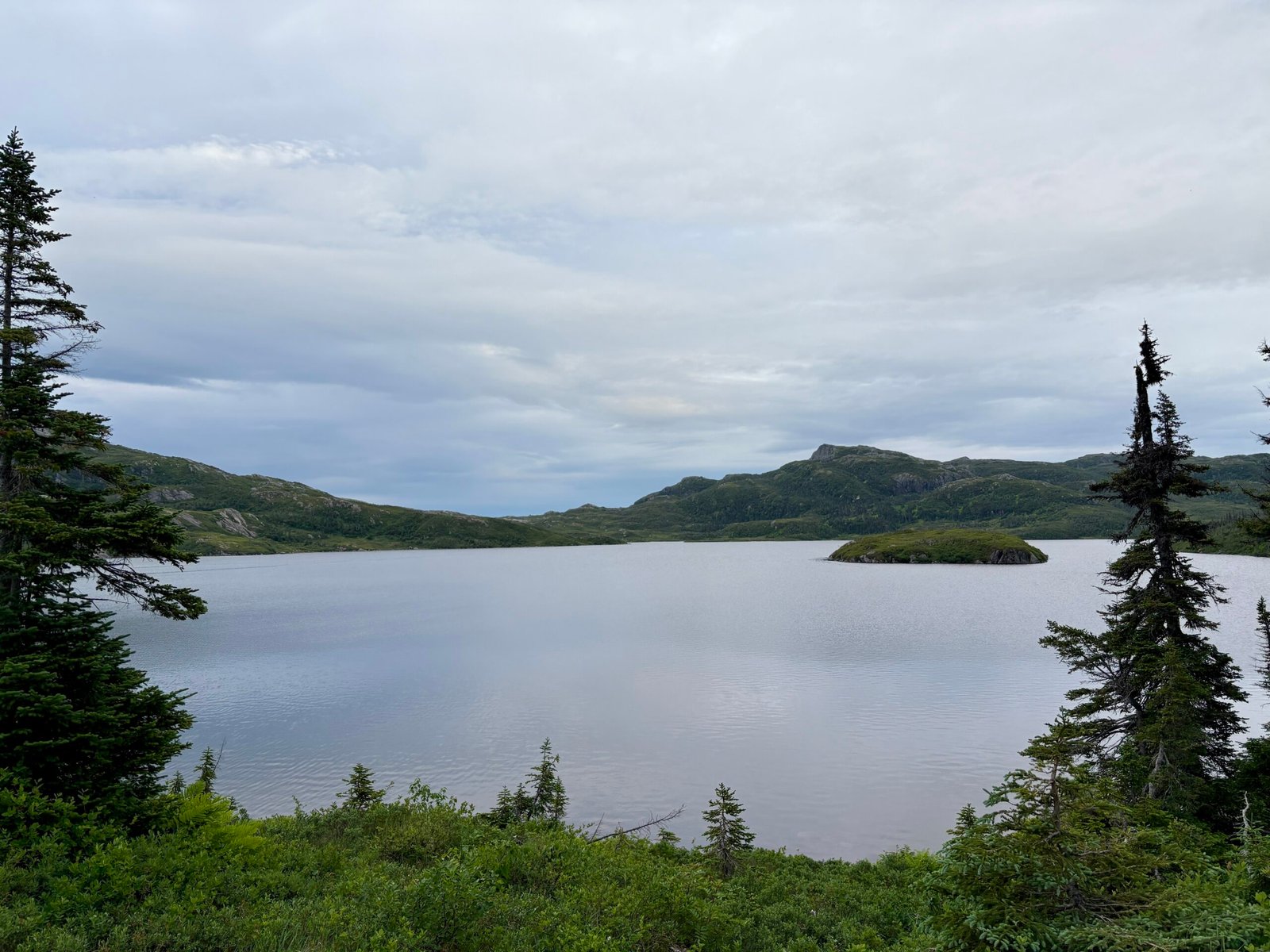 Little Island Pond campsite under a cloudy sky near sunset, with soft light reflecting off the water and a moody, remote feel. A quiet moment on the Long Range Traverse before nightfall.