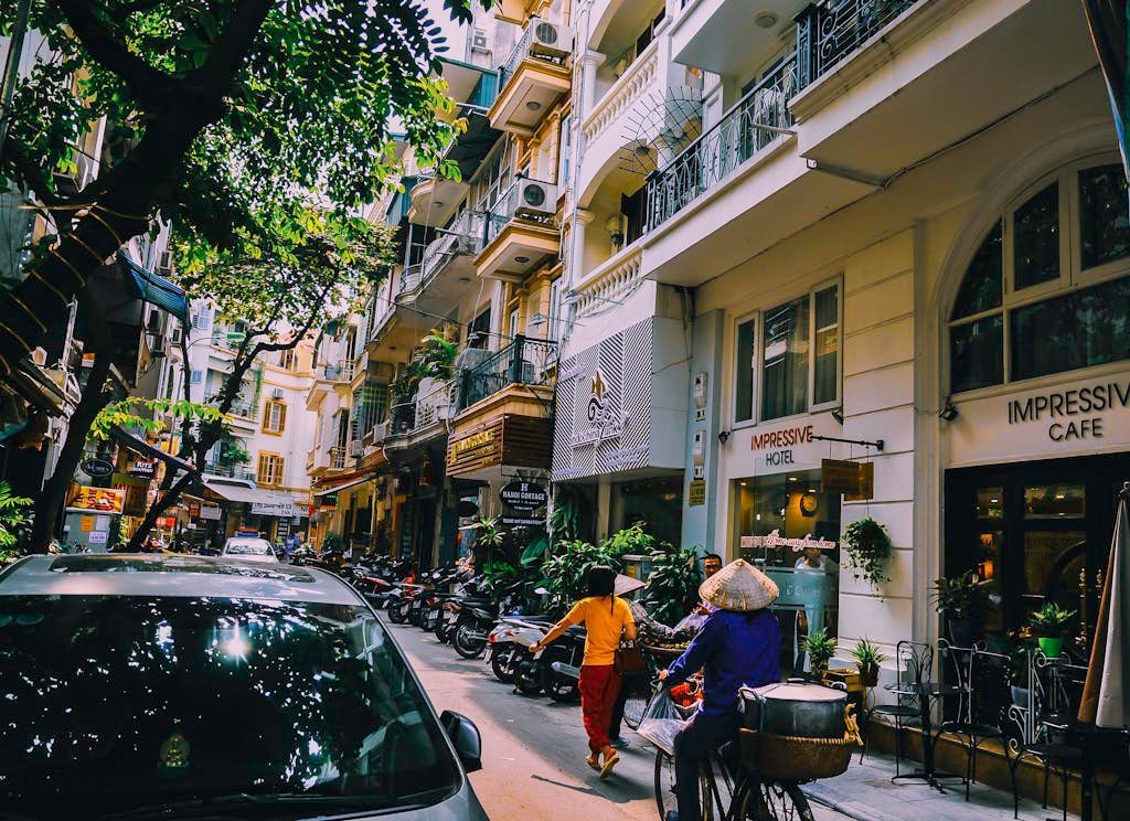 Vibrant street life in Hanoi with locals, cafes, and motorbikes on a sunny day.