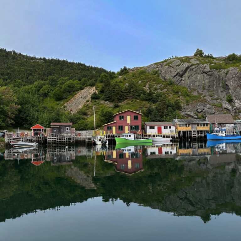 Colorful fishing stages and docked boats line the quiet harbor in Quidi Vidi, with their reflections mirrored perfectly in the still water. Surrounded by forested hills and rocky cliffs just outside St. John’s, this historic village is a must-see stop when exploring things to do in St. John’s Newfoundland.