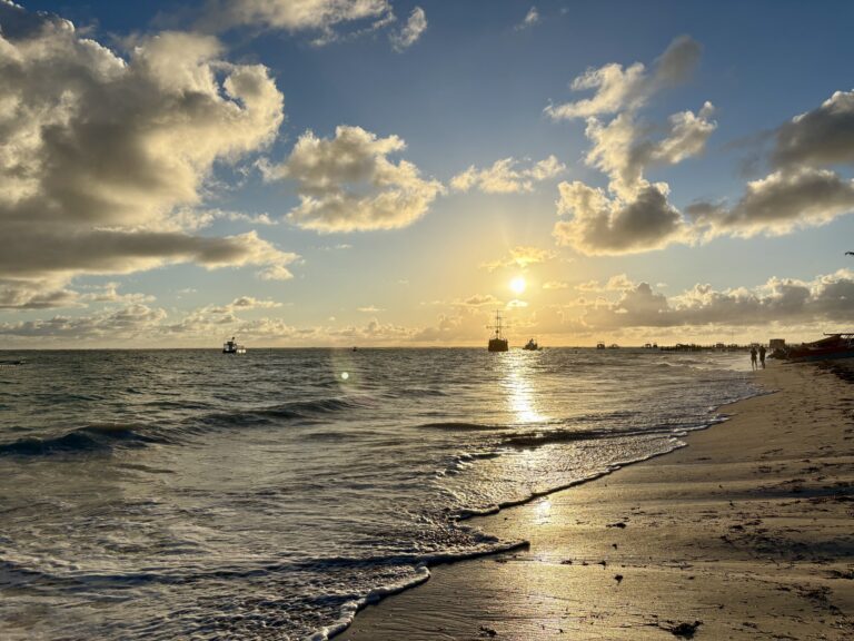 Bavaro beach on Punta Cana right after sunrise on a cloudy day, with a yacht in the distance.