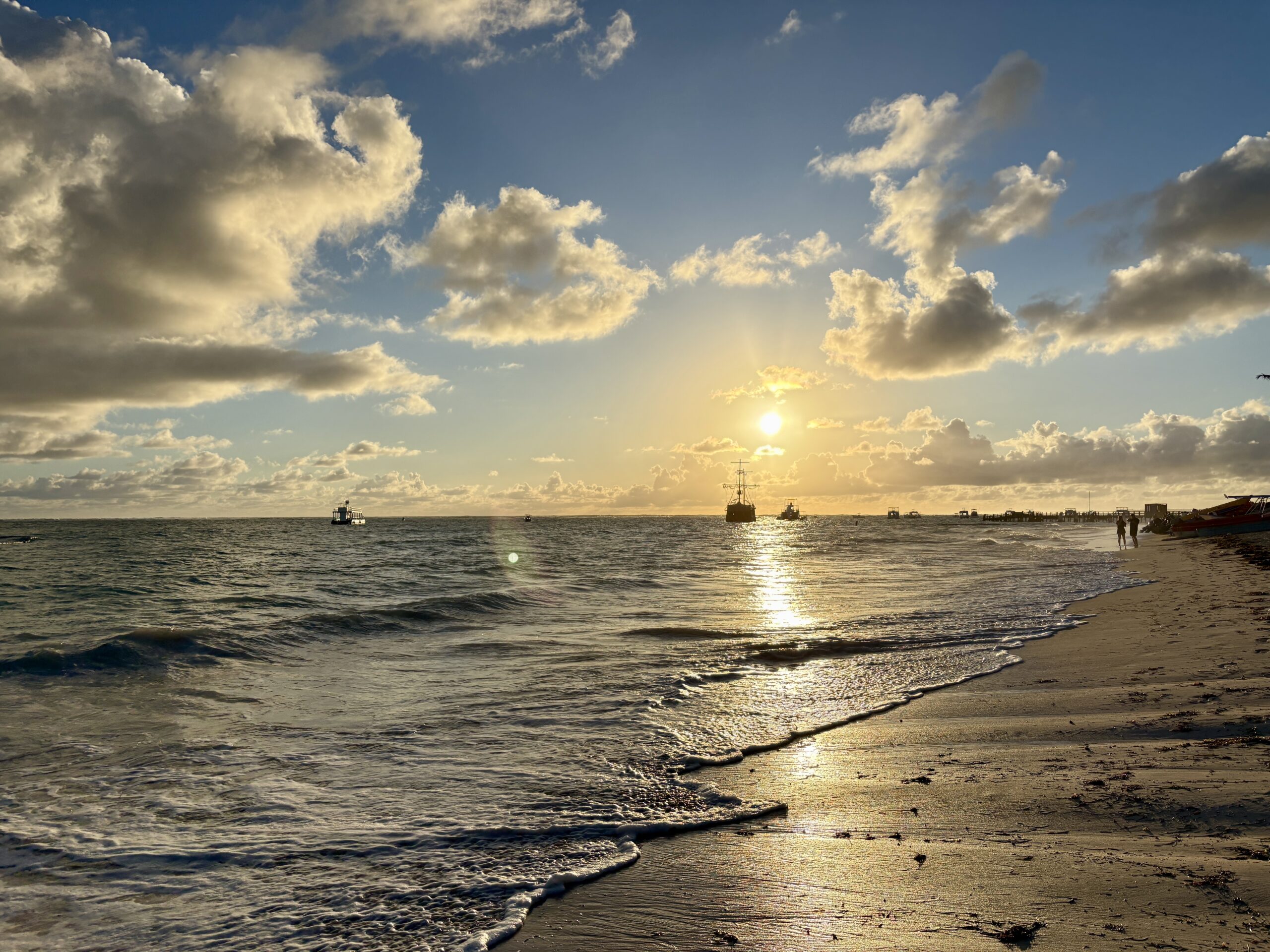 Bavaro beach on Punta Cana right after sunrise on a cloudy day, with a yacht in the distance.