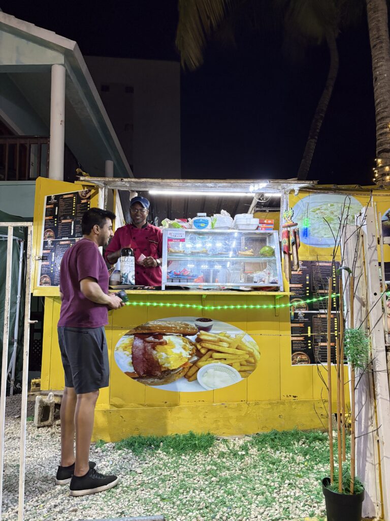 The owner of a food stall stands and smiles at the customer.