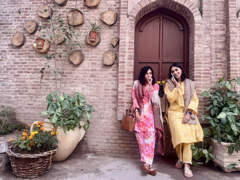 Two women lean against a wall in old Lahore, in colourful clothes, displaying women safety in Pakistan