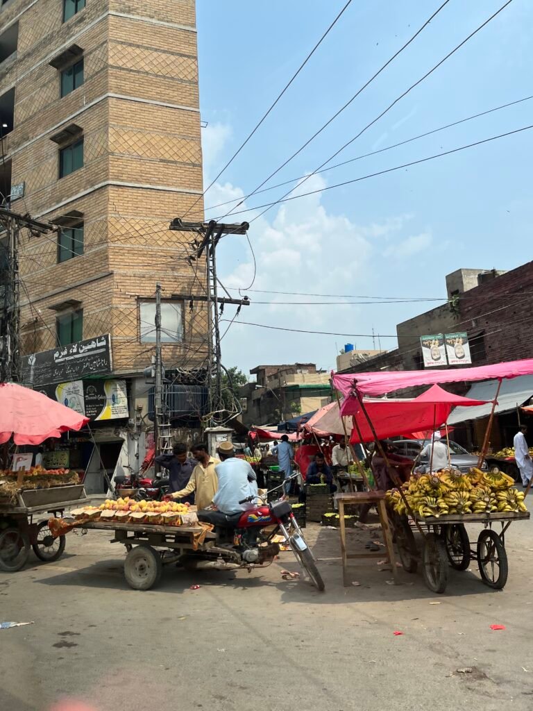 A street vendor in Lahore stands beside a colorful fruit cart piled high with bananas oranges and guavas on a busy roadside. This everyday scene captures the vibrant street life that defines many things to do in Lahore.