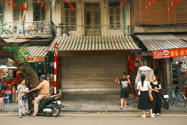 A lively street scene in Hanoi, Vietnam featuring people interacting on a bustling sidewalk, setting the context for where to stay in hanoi