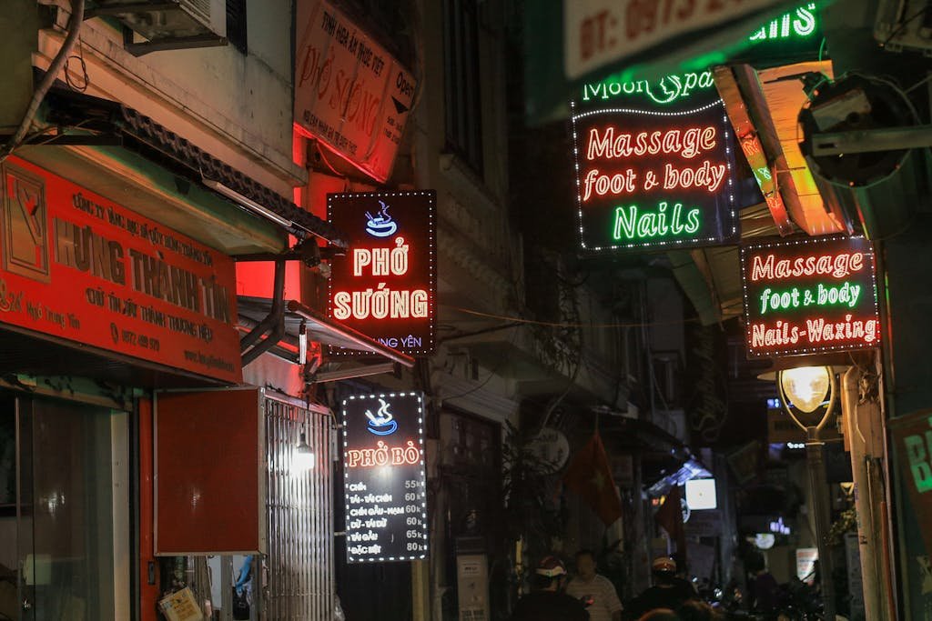 Colorful neon signs illuminate a bustling street in Hanoi, capturing the city's vibrant nightlife, setting the context for where to stay in Hanoi