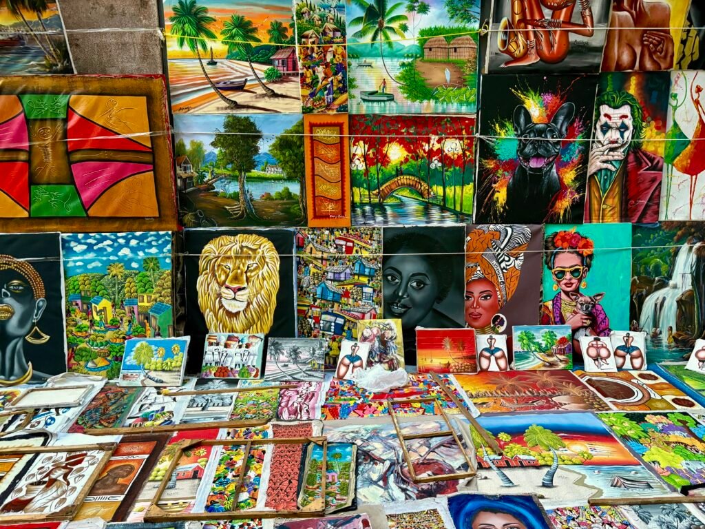 Outdoor art market in Santo Domingo filled with colorful paintings of tropical beaches, palm trees, portraits, wildlife, and Dominican culture. Bright canvases are stacked closely together at a street vendor stall in the Colonial Zone.