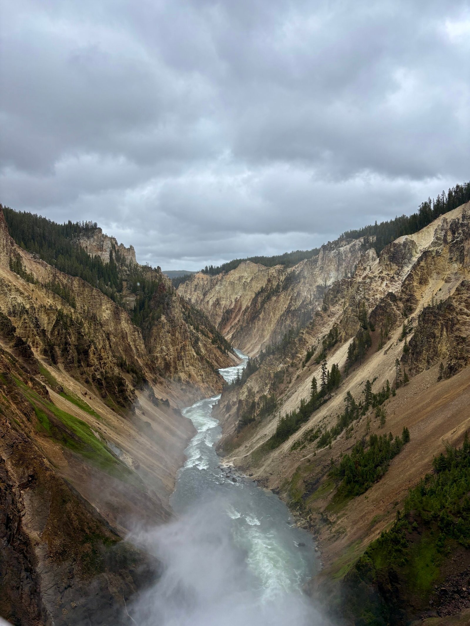 View over the Grand Canyon of the Yellowstone with the river winding between colorful canyon walls on a cloudy day.