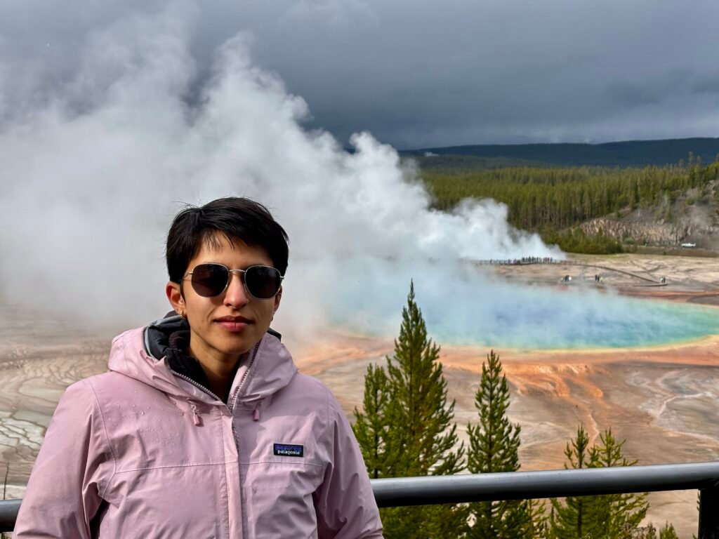 Traveler standing in front of Grand Prismatic Spring as steam rises over the colorful hot spring.