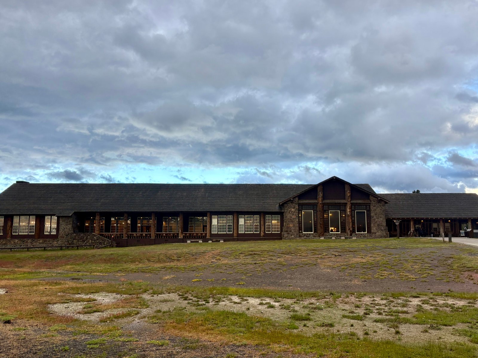 Historic Old Faithful Inn surrounded by open grounds under an evening sky in Yellowstone National Park.