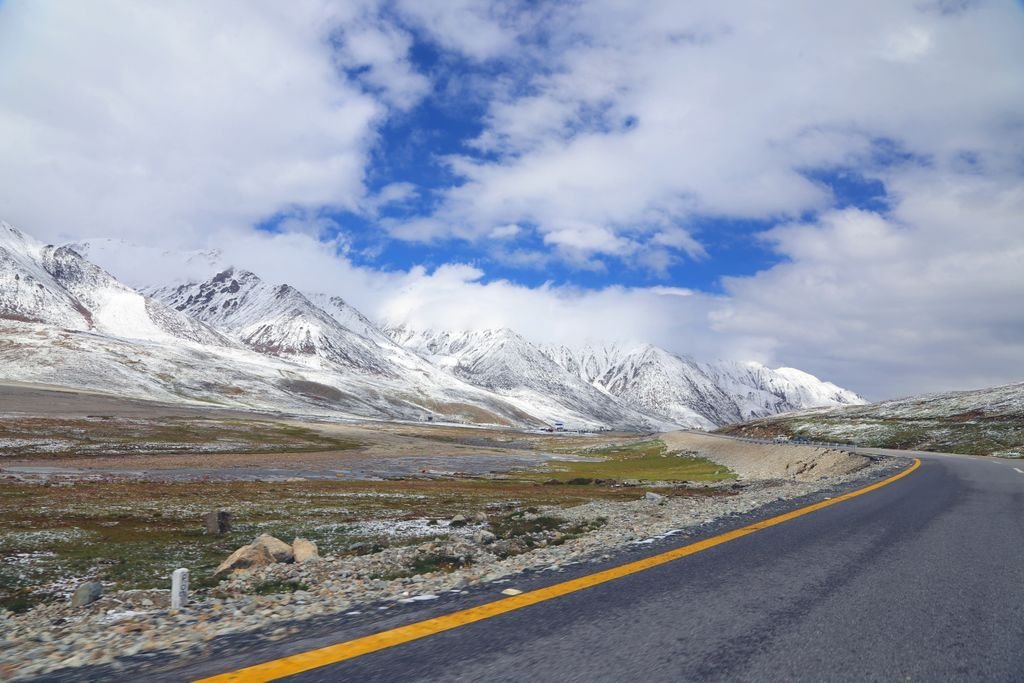 Breathtaking view of a curving road leading to the snow-capped ranges of Gilgit-Baltistan under a vibrant blue sky.